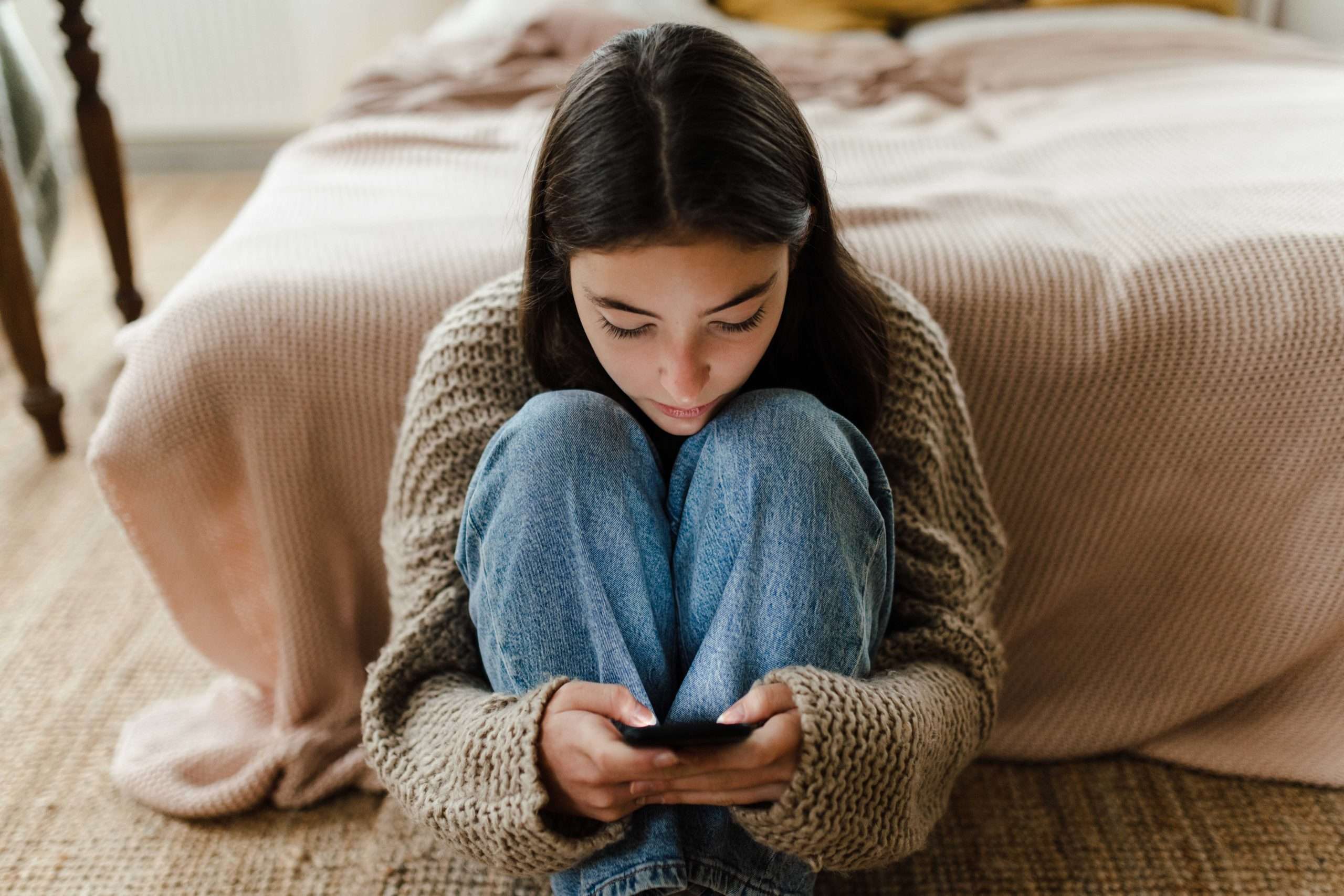 Teenage-girl-sitting-on-the-floor-and-scrolling-her-smartphone