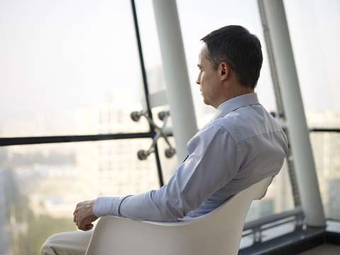 dreamstime_xs_68880847 Businessman thinking in office. Caucasian business executive sitting by the window in a chair thinking in office.