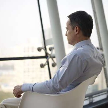 Businessman thinking in office. Caucasian business executive sitting by the window in a chair thinking in office.